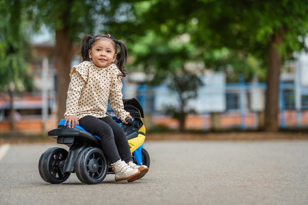 toddler girl riding an electric motorcycle toy in a parkの写真素材
