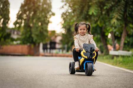 toddler girl riding an electric motorcycle toy in a park with sunlightの写真素材