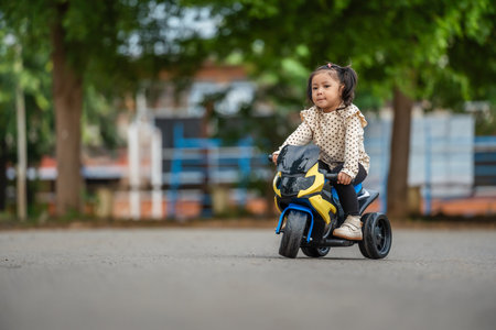 toddler girl riding an electric motorcycle toy in a parkの写真素材