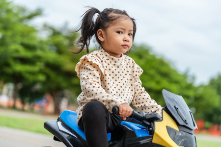 toddler girl riding an electric motorcycle toy in a parkの写真素材