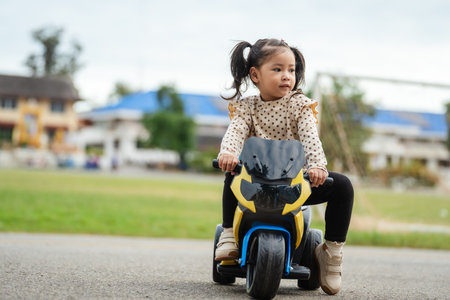 toddler girl riding an electric motorcycle toy in a parkの写真素材