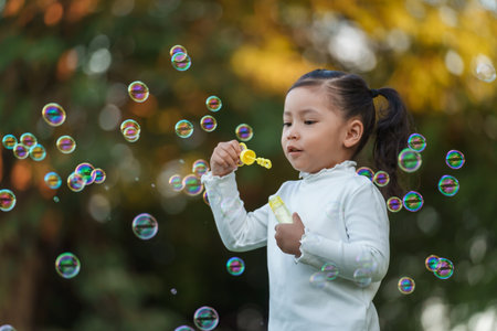 happy toddler girl blowing soap bubbles in the park