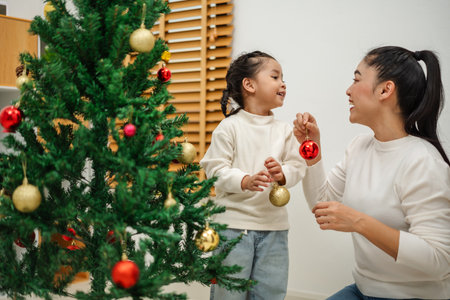 happy mother and toddler girl decorating Christmas tree with toy ball at homeの写真素材