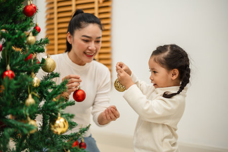 happy mother and toddler girl decorating Christmas tree with toy ball at homeの写真素材
