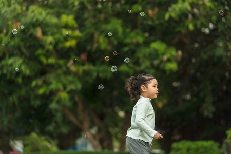 happy toddler girl running and playing soap bubble in the park