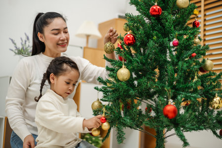happy mother and toddler girl decorating Christmas tree with toy ball at homeの写真素材