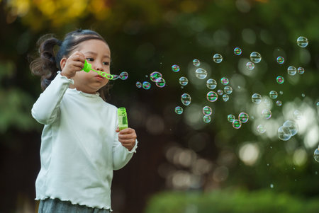 happy toddler girl blowing soap bubbles in the parkの写真素材
