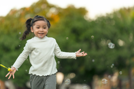 happy toddler girl running and playing soap bubble in the parkの写真素材