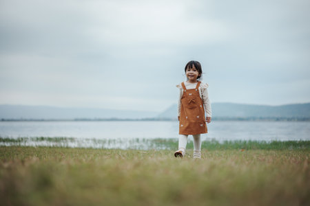 happy toddle girl walking on a grass field near the riverの写真素材