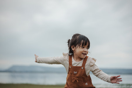 happy toddle girl palying and dancing on a grass field near the riverの写真素材