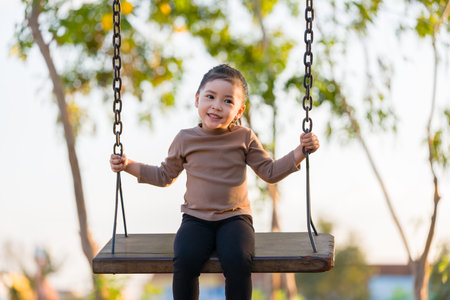 cheerful child girl playing on a swing at playgroundの写真素材