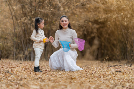 Mother and child girl bonding while playing with butterfly nets outdoors in dry forest.の写真素材
