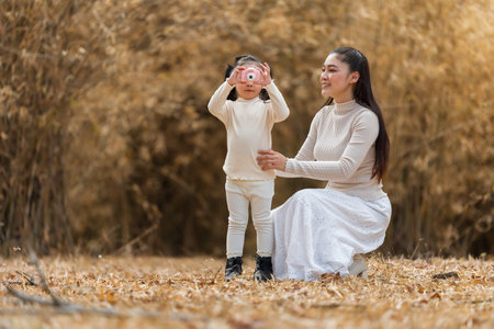 Mother teaching child girl how to use a pink toy camera in the park or dry bamboo forestの写真素材