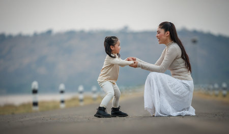 happy mother and child girl holding hands on a road near the lakeの写真素材