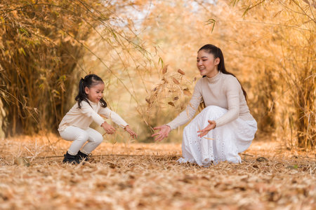 Mother and child girl having fun throwing dry leaves in the air during autumn in the golden bamboo forestの写真素材