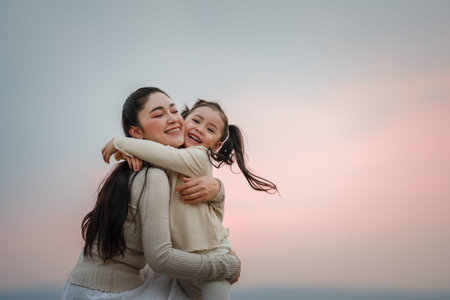 Heartwarming moment of mother and child girl hugging at a sunsetの写真素材