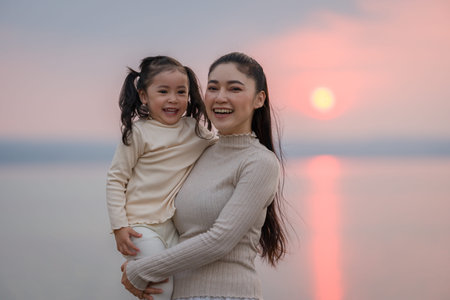 Loving mother holding her child girl while watching the sunset glowの写真素材