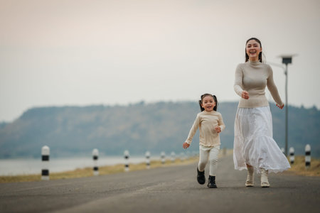 Mother and child girl walking and playing on a scenic road during dusk near the riverの写真素材