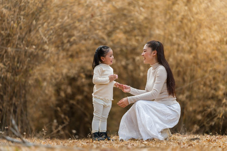 Mother teaching child girl how to use a toy camera in the park or dry bamboo forestの写真素材