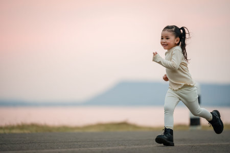 Energetic little child girl running happily on an open road by the water at sunsetの写真素材