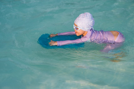 preschool child girl learning to swim with board in the swimming pool