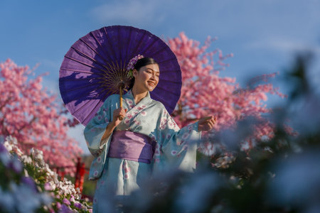 woman in yukata (kimono dress) holding umbrella with sakura flower or cherry blossom blooming in the...