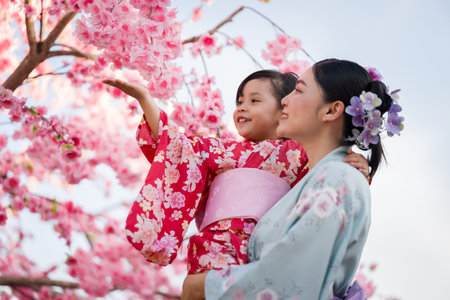 woman and child girl in yukata (kimono dress) with sakura flower or cherry blossom blooming in the...