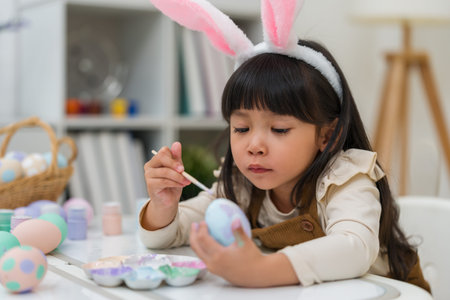 preschool child girl wearing bunny ears painting and decorating colorful egg at the home on easter dayの写真素材