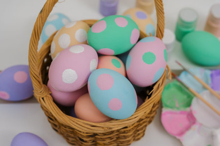 many colorful pastel decorated easter eggs in a small wooden basket and watercolor painting tool on...