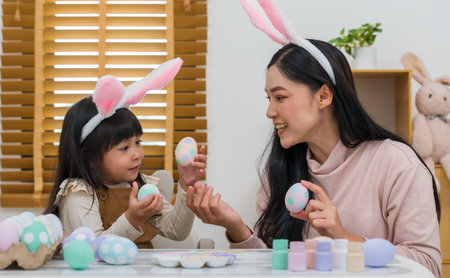 mother and preschool child girl wearing bunny ears holding colorful egg while celebrating together...