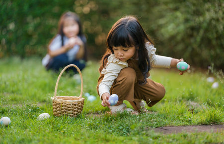 two child girl playing together and hunting for Easter eggs into basket on green grass in the garden