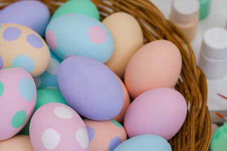 many colorful pastel decorated easter eggs in a small wooden basket and watercolor painting tool