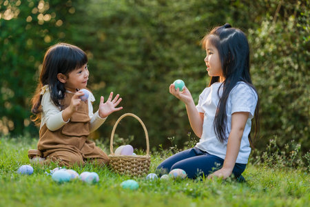 two child girl playing together and hunting for Easter eggs into basket on green grass in the gardenの写真素材