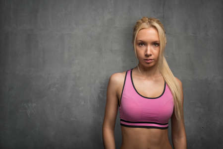 Athletic sporty young woman in a pink top folded her arms on a gray background.の写真素材