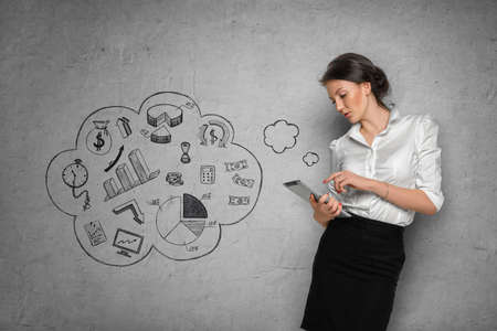 Young pretty woman in office cloth with tablet on concrete wall background with business sketchesの写真素材