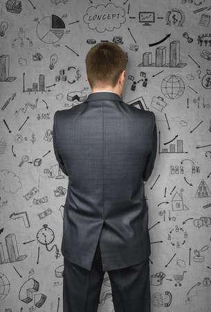 Businessman in a suit on concrete wall with sketches. Financial concept.の写真素材