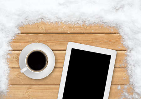 Top view of one cup of coffee and tablet on a wooden surface covered with snowの写真素材