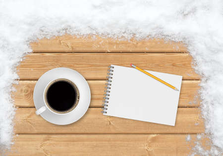 A cup of coffee, a pencil and a notebook, viewed from the top, on the planks covered with snowの写真素材