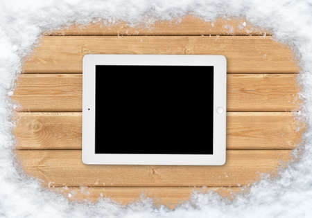 Top view white tablet on a wooden surface covered with snow along the edgesの写真素材