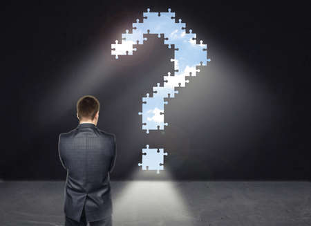 A businessman standing in front of the wall with a big question mark looking like a way out of the...