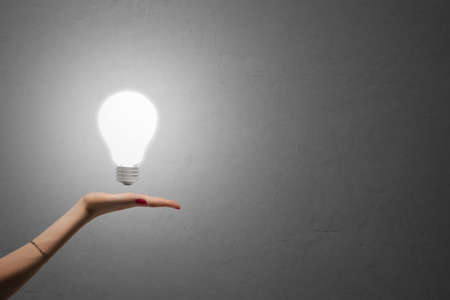 Glowing light bulb on a palm, a concrete wall in the background.