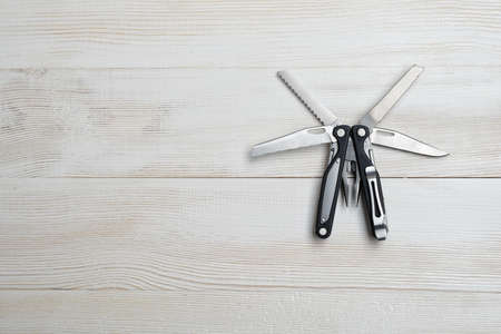 Multi tool with black handles on white wooden background. Top view of desktop