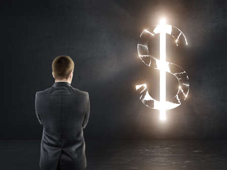 Businessman standing in front of concrete wall with bright dollar sign. Financial and business concept.の写真素材
