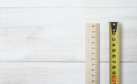 Top view of  tape measure and ruler on white wooden DIY workbench. Flat lay