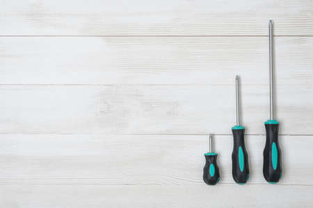 A set of three screwdrivers different size lying on a white wooden surfaceの写真素材