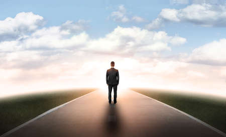 Back view of a businessman walking straight on his way on an asphalt road during the daytime.