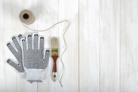 An art composition featuring of gloves, brush and a twine lying on a white wooden surface. Tools.