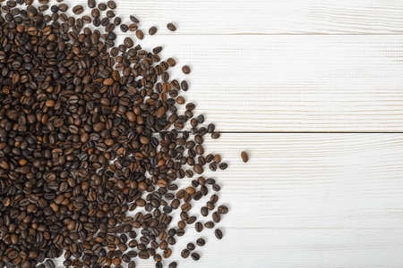 Coffee beans scattered on left side of light beige wooden surfaceの写真素材