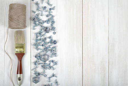 Top view of screws, nuts, a brush and twine on wooden DIY workbench with open space on the right side.の写真素材