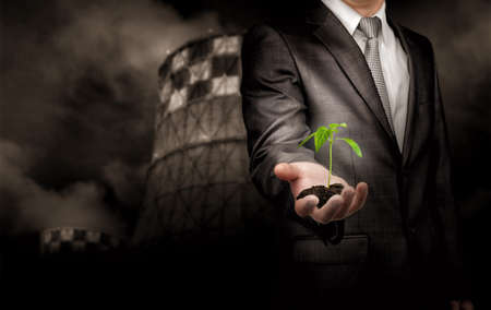 Sprout growing on the ground in hand of businessman standing over thermal power plant background. Concept.の写真素材